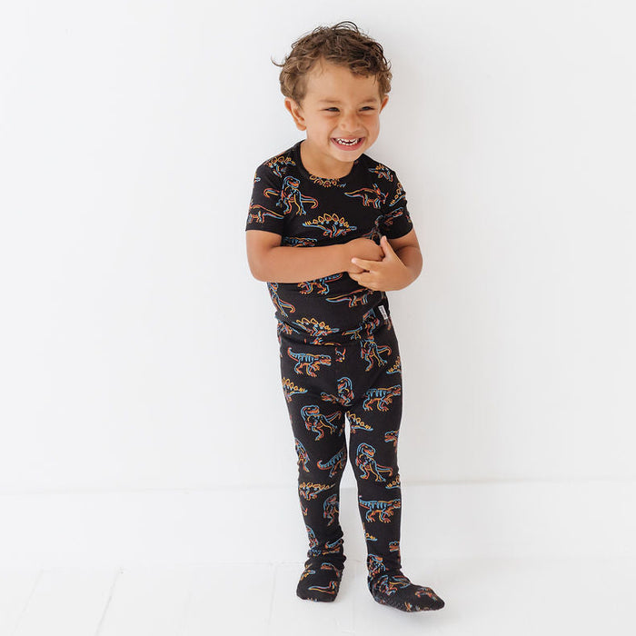 Child wearing a black pajama set with dinosaur print on a white background