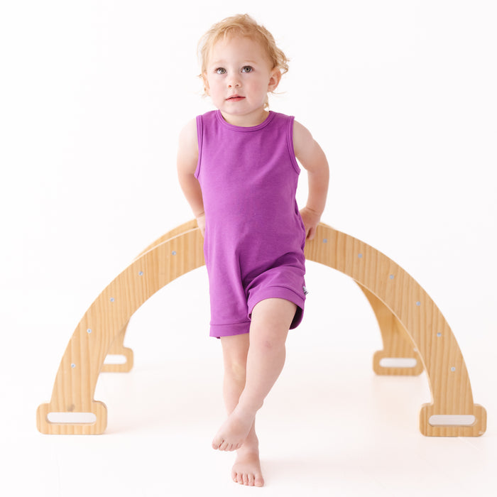 Child sitting on a wooden arch toy with a white background
