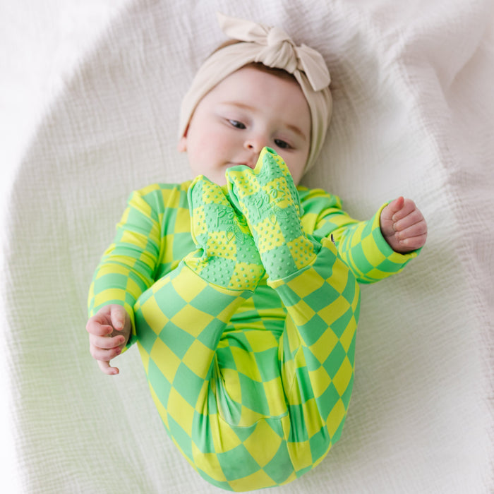 Baby wearing a green and yellow checkered outfit with a matching headband on a white blanket.