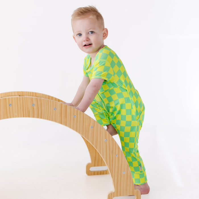 Child in a green checkered outfit climbing on a wooden arch