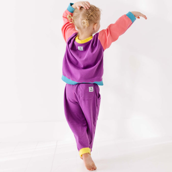 Child wearing a colorful outfit with a purple top and pants on a white background