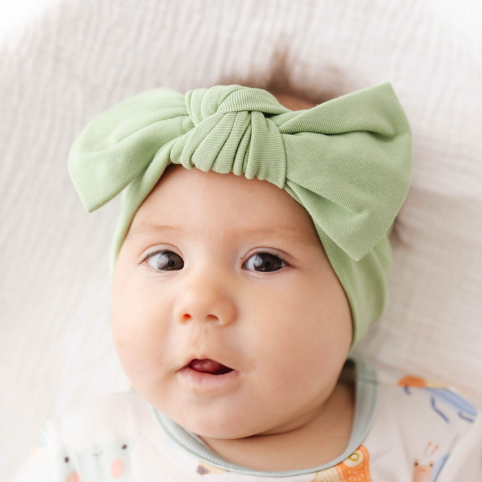 Baby wearing a green headband with a bow, sitting on a white surface.