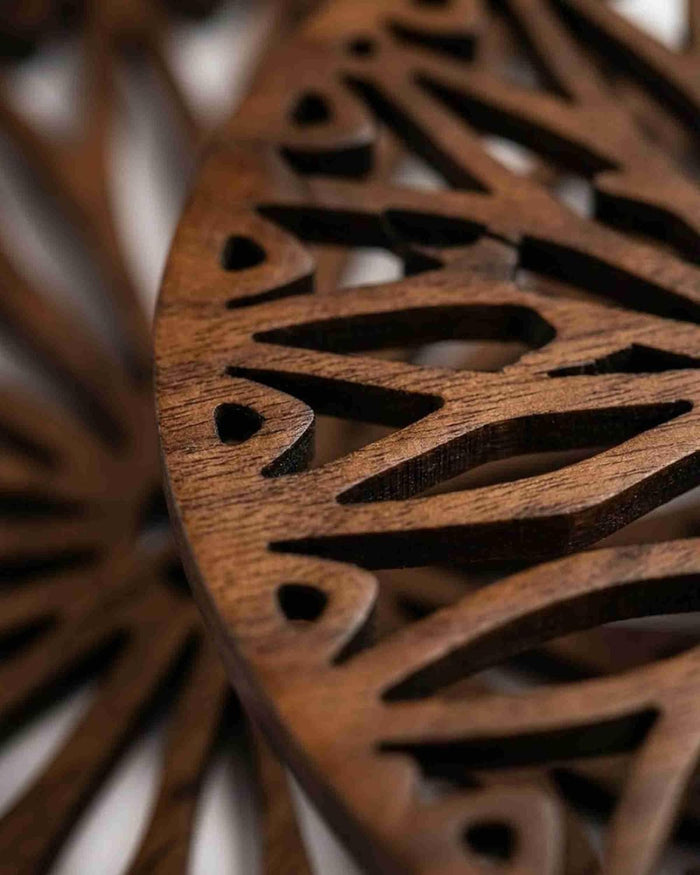 Dark brown wooden trivet close-up with curved geometric laser-cut pattern and rich wood grain