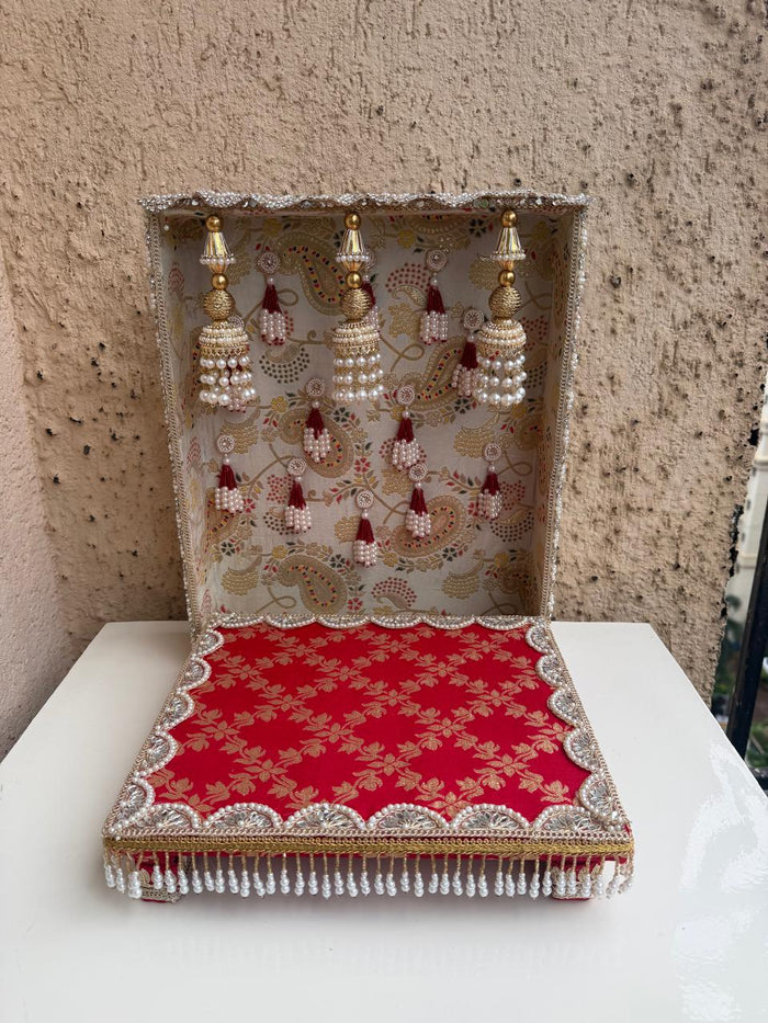 Decorative idol backdrop stand with gold frame, red patterned mat, and hanging decor