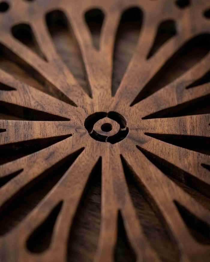 Close-up of dark brown round wooden trivet center with sunflower spoke cutouts