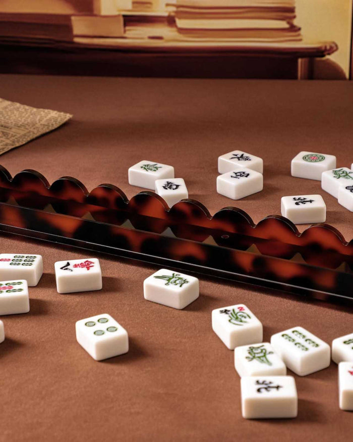 Tortoise shell acrylic mahjong tile rack with scattered white tiles on tabletop