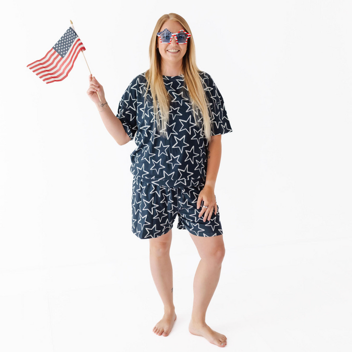 Person wearing a navy blue outfit with white star pattern, holding an American flag and sunglasses on a white background