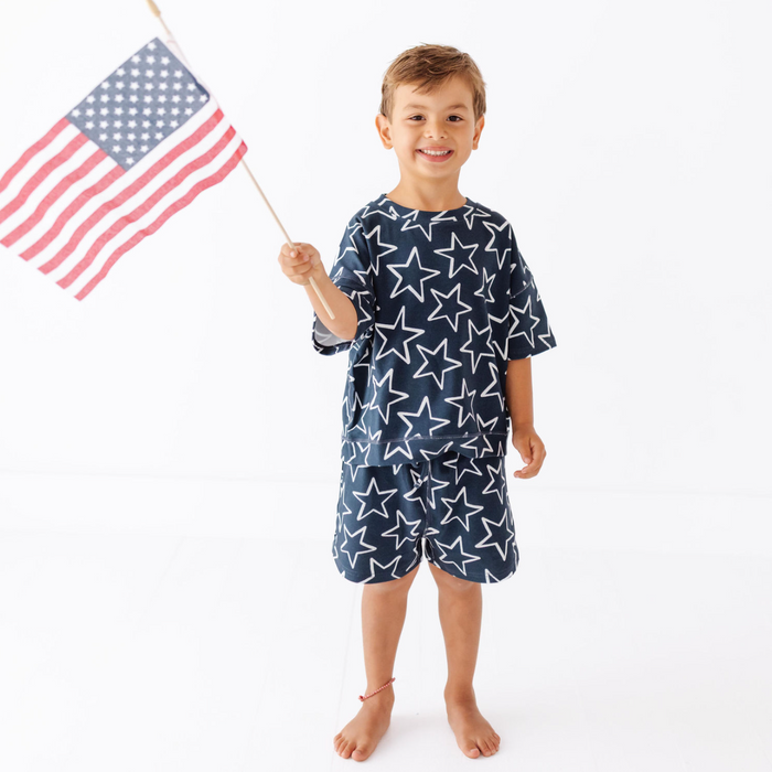 Child wearing a star-patterned outfit holding an American flag on a white background