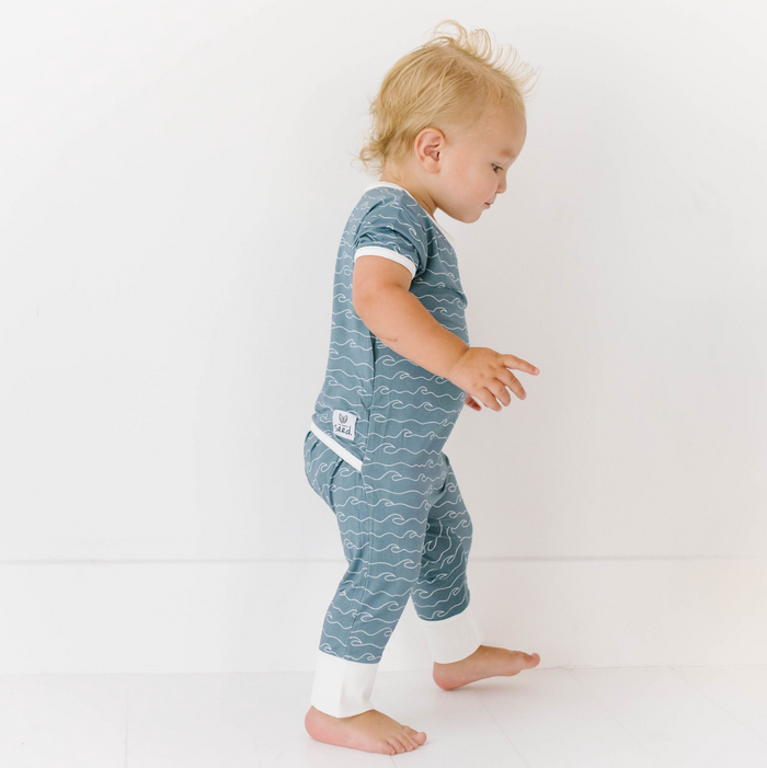 A toddler wearing a blue and green striped bamboo fabric romper with short sleeves and long leg cuffs.